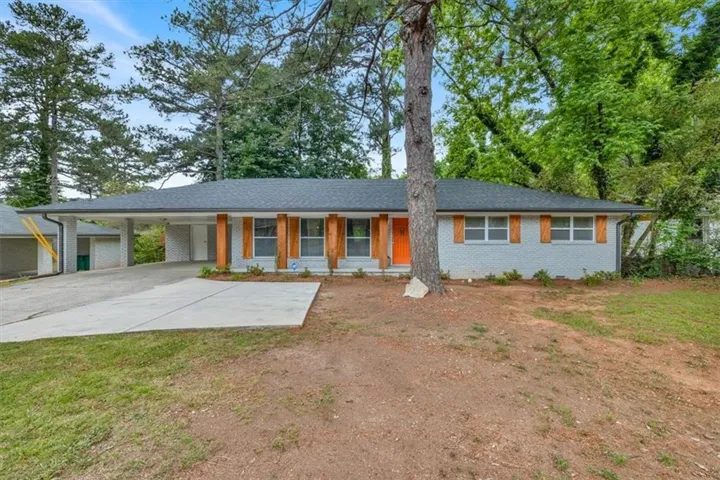 Ranch-style residence featuring a gray brick exterior, dark shingle roof, and a prominent orange front door
