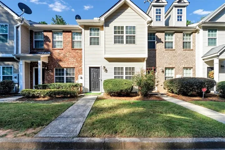 Brick and siding exterior with multiple window styles, established landscaping, and a concrete pathway