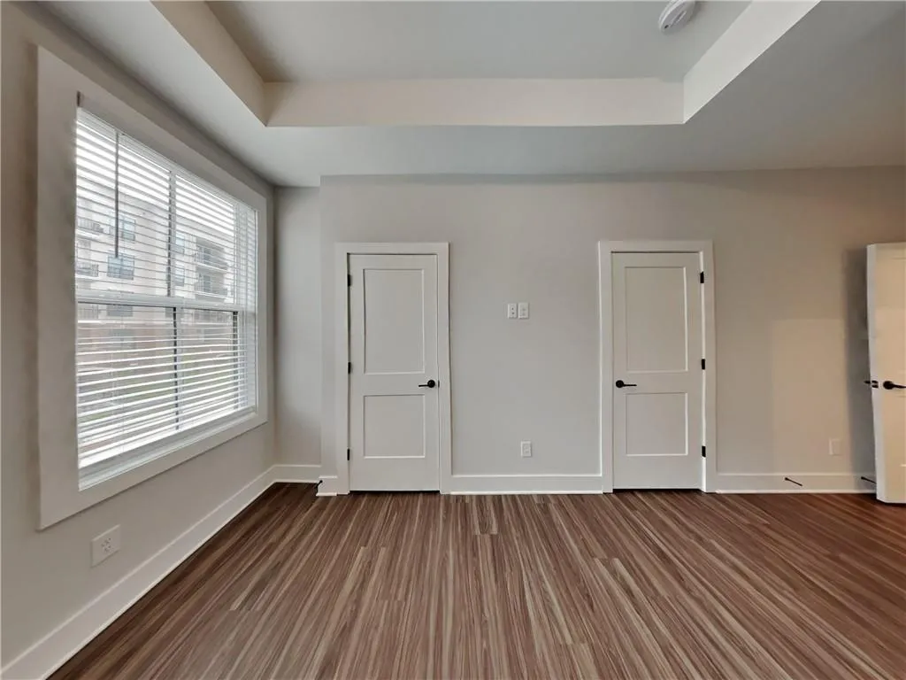 Unfurnished bedroom with a tray ceiling and dark wood finished floors