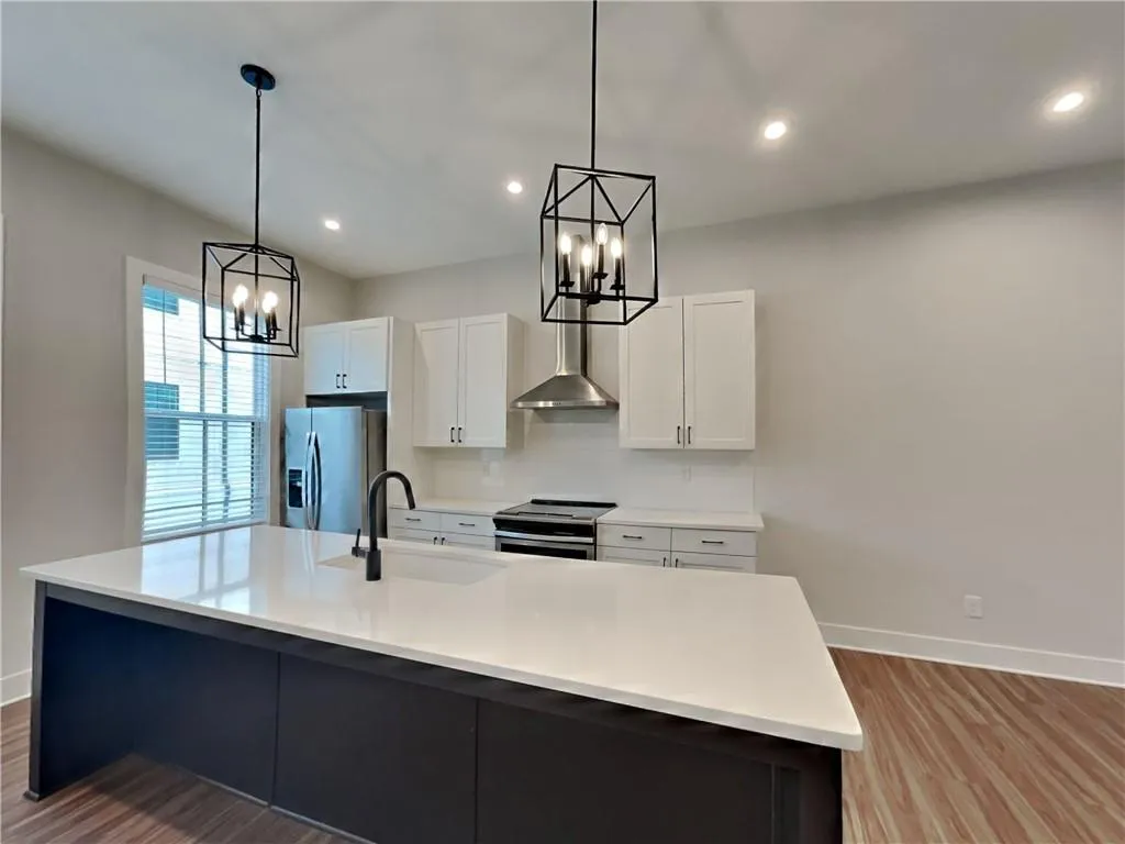 Kitchen featuring light wood finished floors, appliances with stainless steel finishes, wall chimney range hood, white cabinetry, and recessed lighting