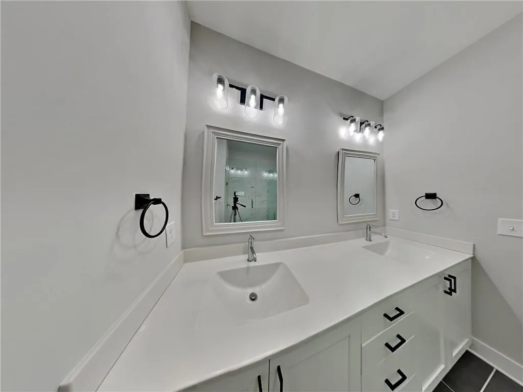 Full bath with a shower stall, double vanity, and dark tile patterned flooring