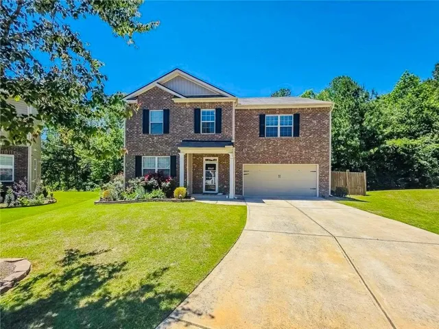 Brick exterior with dark shutters, covered front entry, attached garage, concrete driveway, and manicured landscaping