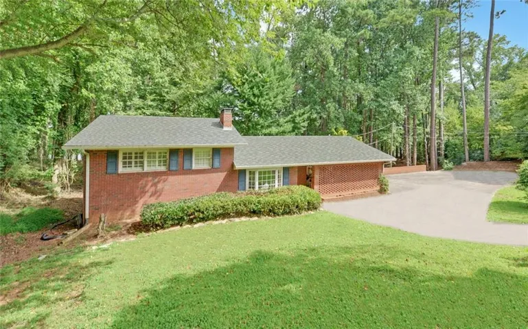 Red brick exterior with blue shutters, a dark shingle roof, a paved driveway, and established landscaping