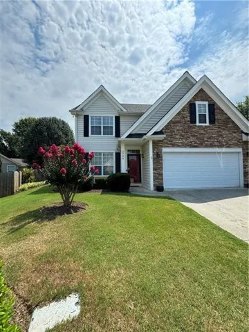 Two-story residence featuring a stone and siding facade, a two-car garage, and a red entry door