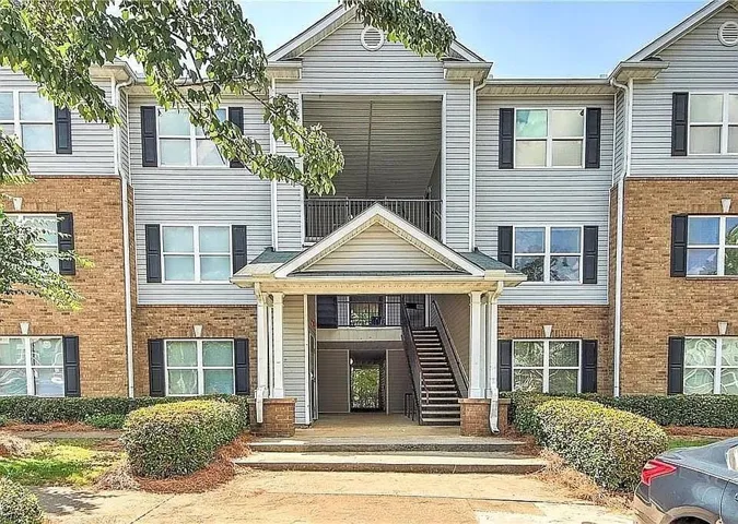 Multi-story residential building featuring brick and siding exterior, multiple windows with dark shutters, and an inviting covered entrance