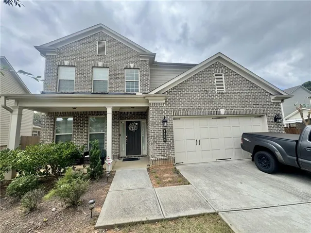 Two-story brick facade residence featuring a covered front porch, a two-car garage, and a concrete driveway