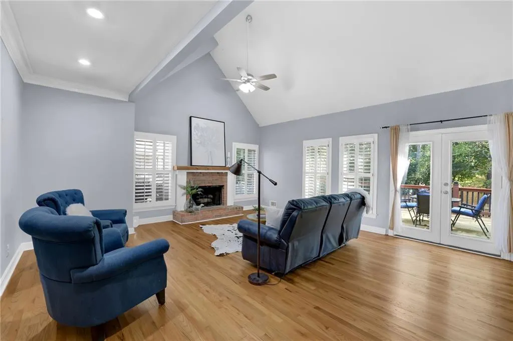 Living room featuring a brick fireplace, light hardwood floors, high vaulted ceiling, and ceiling fan