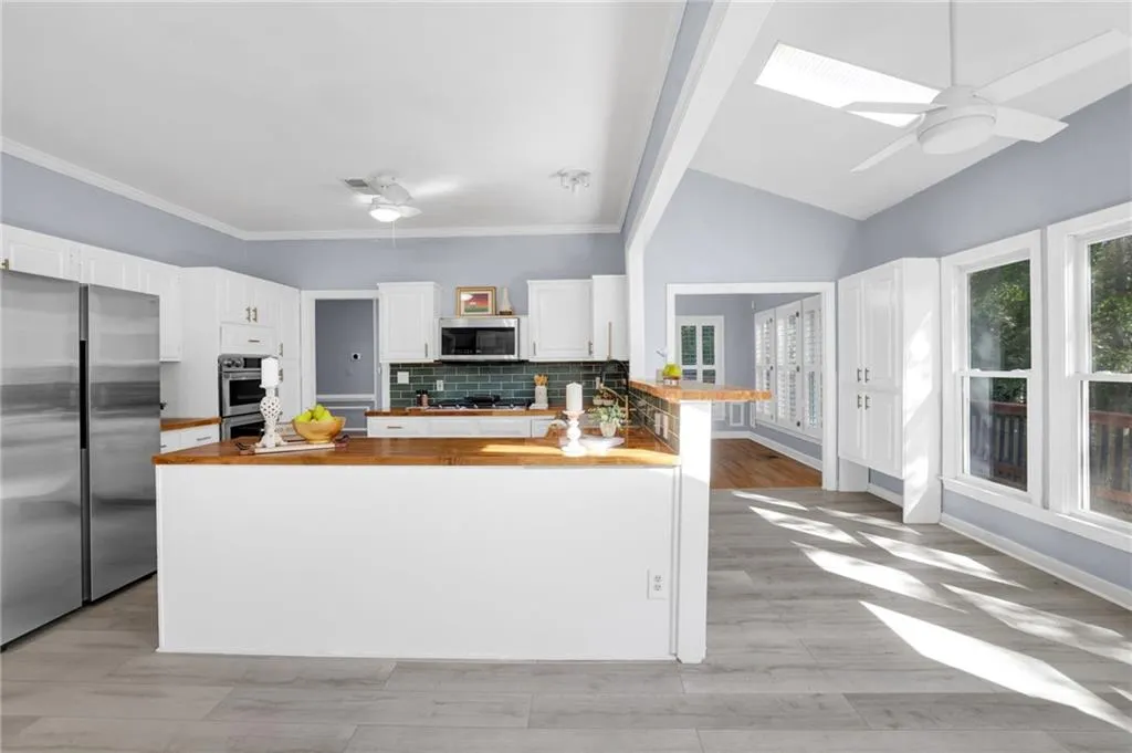Kitchen featuring appliances with stainless steel finishes, kitchen peninsula, white cabinetry, and wood counters