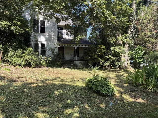 Two-story facade with vertical siding, covered front porch, and mature trees