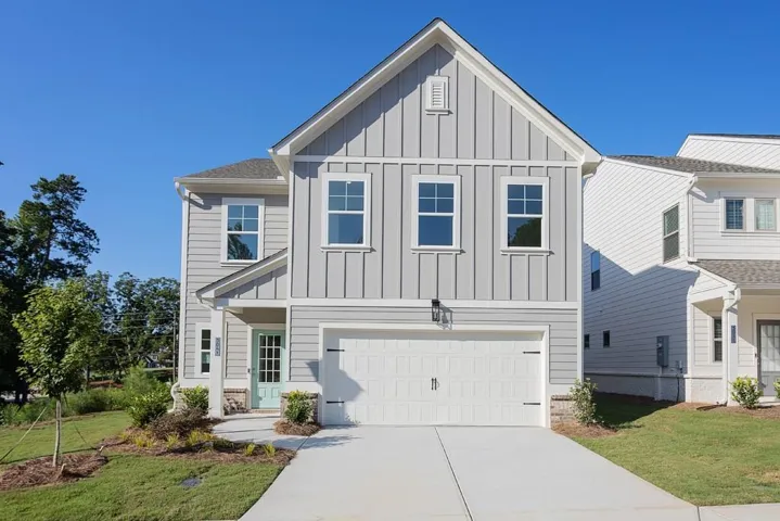 Light gray siding exterior with board and batten gables, covered entry porch, light blue paneled front door, attached garage with white door, and concrete driveway