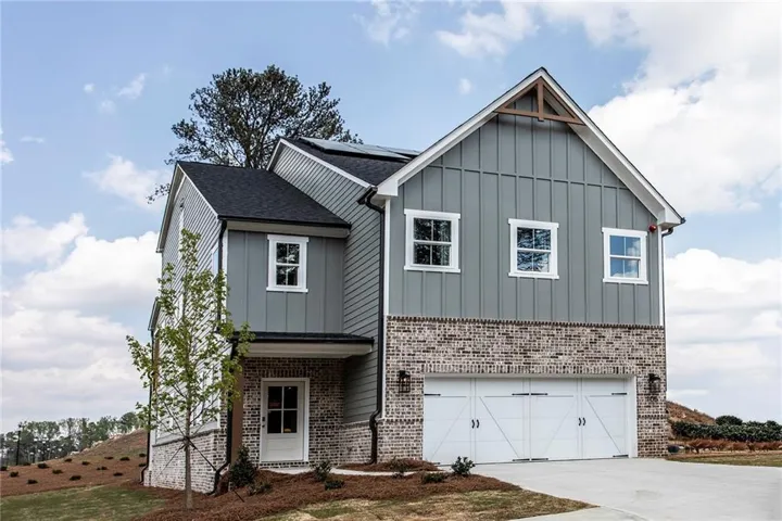 Two-story exterior with board and batten siding, brick accents, white trim windows, a two-car garage, and a covered entry