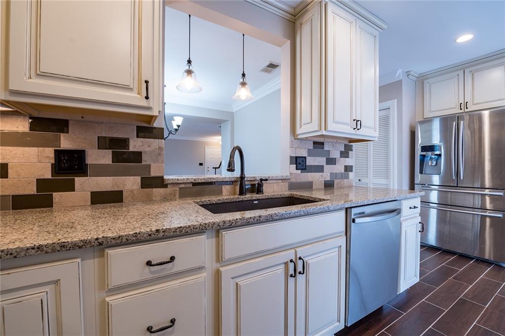 Kitchen with sink, light stone countertops, appliances with stainless steel finishes, backsplash, and pendant lighting