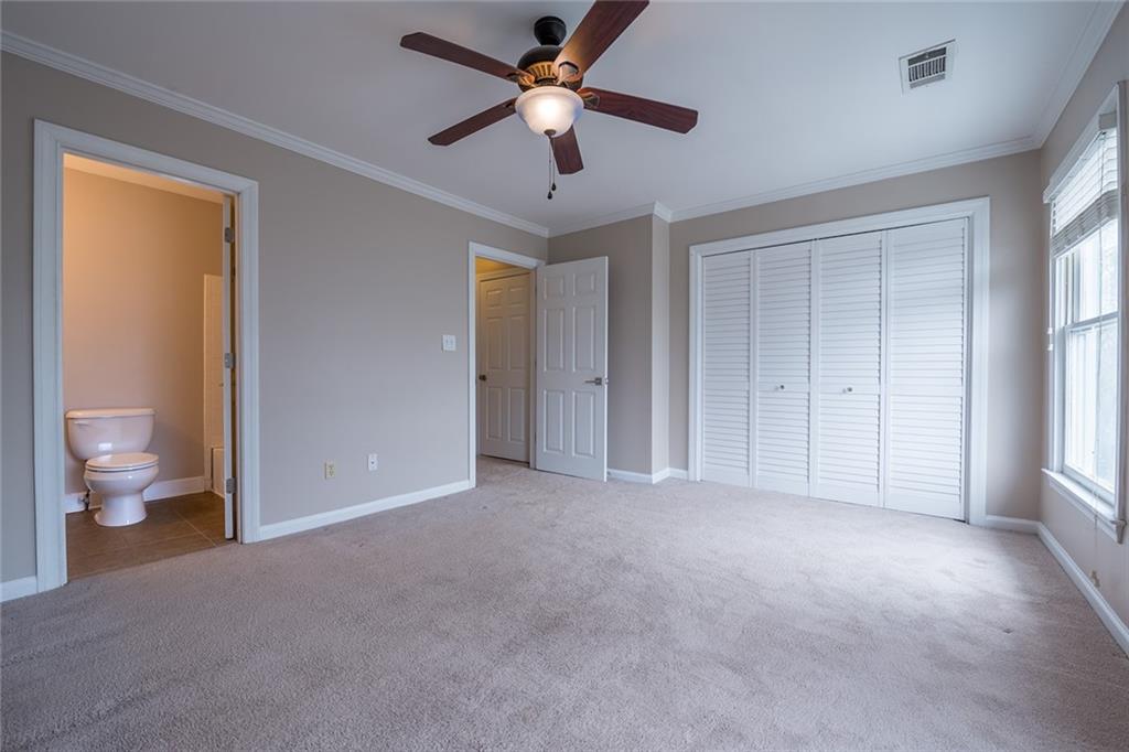 Unfurnished bedroom with light carpet, a closet, ornamental molding, connected bathroom, and ceiling fan