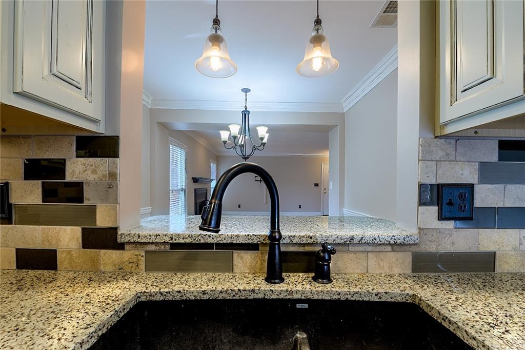 Kitchen featuring white cabinetry, a chandelier, hanging light fixtures, ornamental molding, and light stone counters