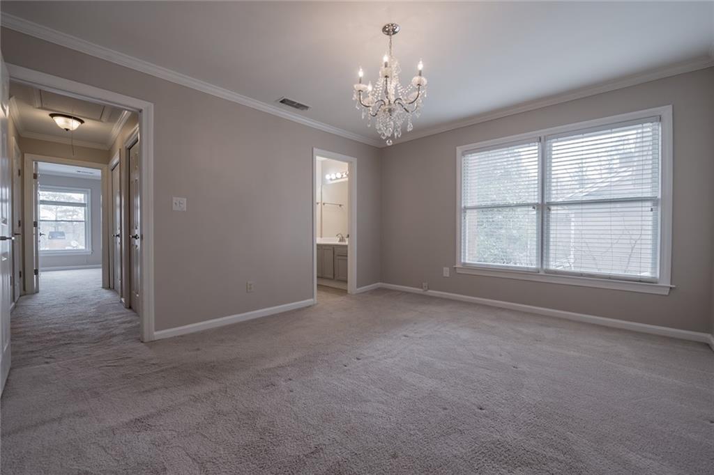 Carpeted empty room with a wealth of natural light, a chandelier, and crown molding
