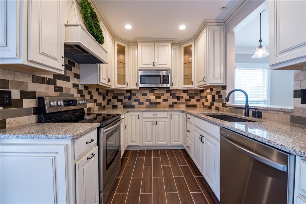 Kitchen with sink, custom range hood, appliances with stainless steel finishes, ornamental molding, and pendant lighting