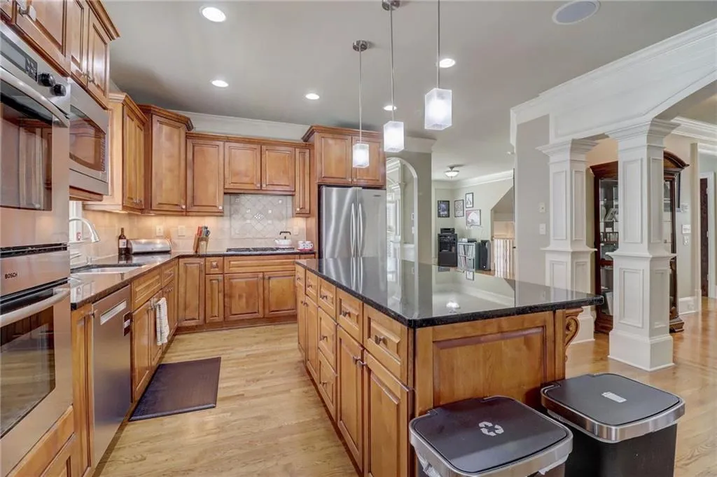 Kitchen featuring light hardwood / wood-style floors, ornate columns, stainless steel appliances, dark stone countertops, and backsplash
