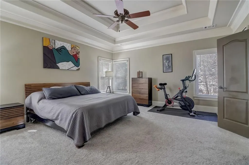 Carpeted bedroom with ornamental molding, ceiling fan, and a raised ceiling