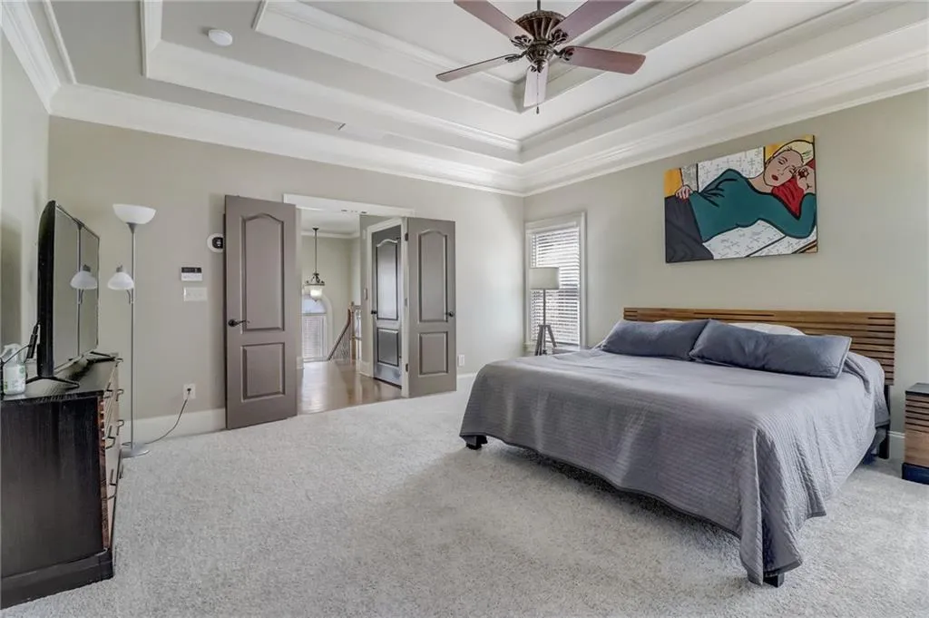 Carpeted bedroom featuring ceiling fan, a tray ceiling, and crown molding