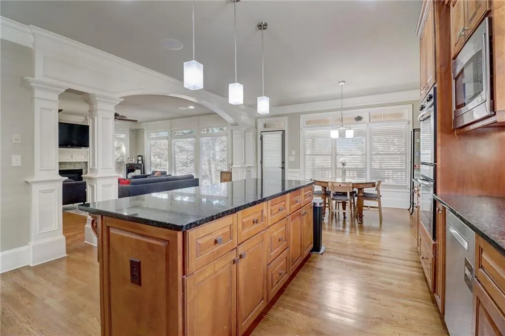 Kitchen featuring light hardwood / wood-style floors, stainless steel appliances, hanging light fixtures, a center island, and ornate columns