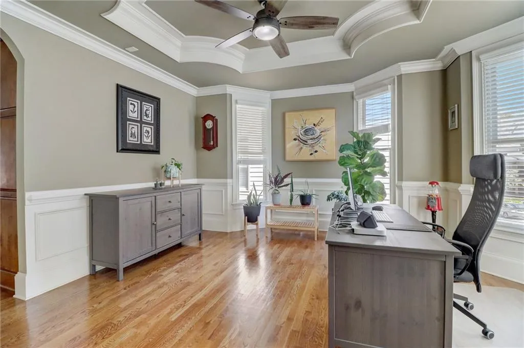 Office space featuring a raised ceiling, ceiling fan, a healthy amount of sunlight, and light hardwood / wood-style flooring