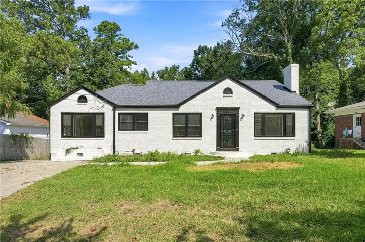 White brick exterior with a dark shingle roof, black window frames, and a prominent front door with a decorative screen
