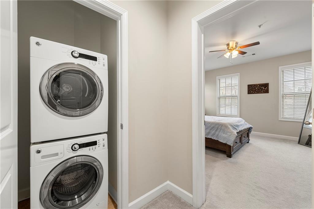 Clothes washing area with light carpet, stacked washer and clothes dryer, and ceiling fan