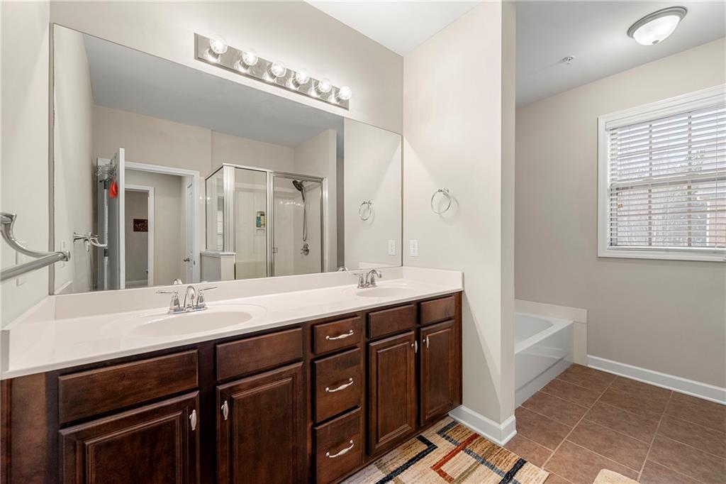 Bathroom featuring dual sinks, vanity with extensive cabinet space, tile flooring, and independent shower and bath