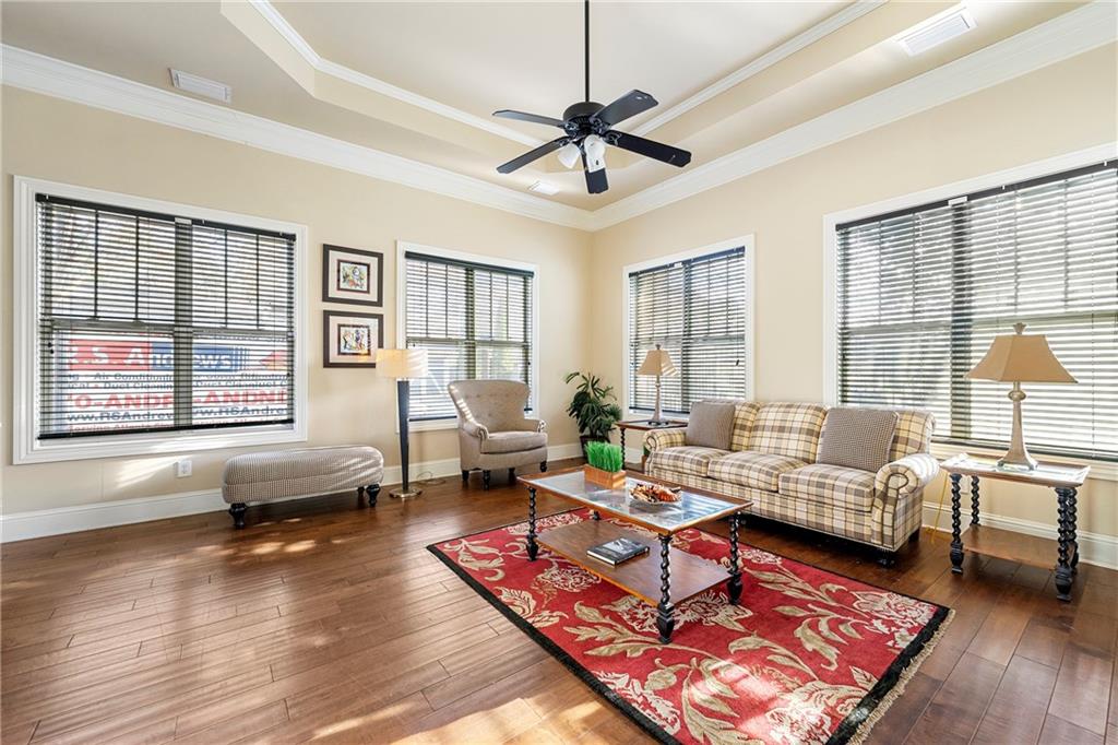 Living room featuring ornamental molding, a tray ceiling, dark wood-type flooring, and ceiling fan