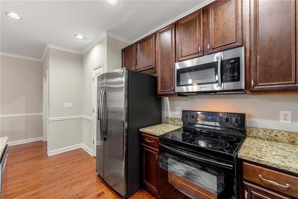 Kitchen featuring ornamental molding, light wood-type flooring, light stone countertops, and appliances with stainless steel finishes