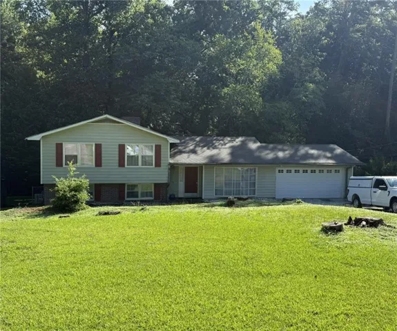 Mint green siding exterior featuring a split-level design, red entry door, attached garage with window inserts, and a prominent front lawn