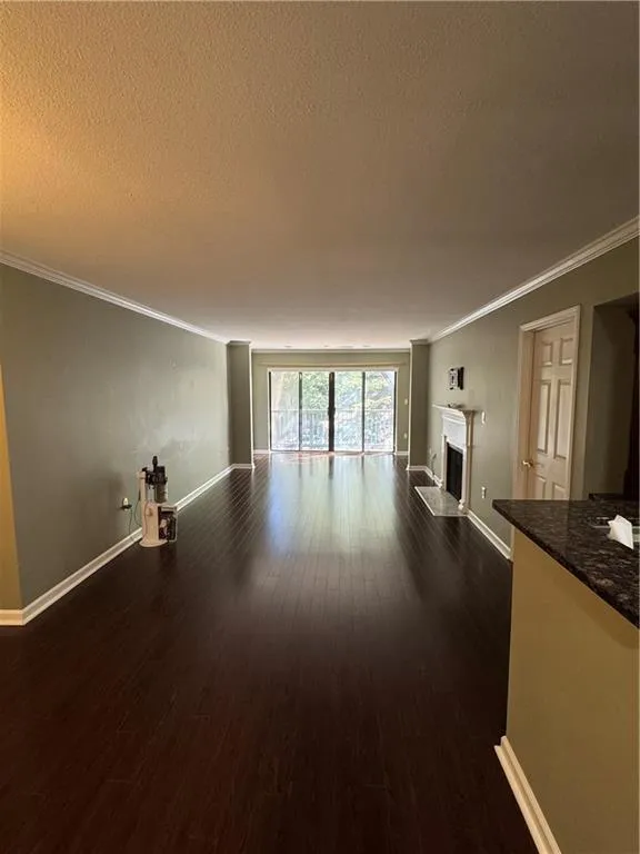 Unfurnished living room featuring dark wood-style flooring, a fireplace, ornamental molding, and a textured ceiling