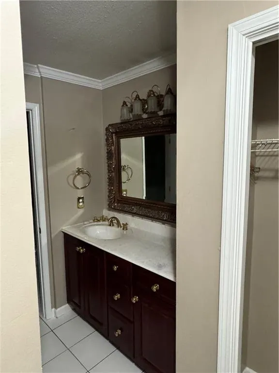 Bathroom featuring light tile patterned floors, vanity, a textured ceiling, ornamental molding, and a walk in closet