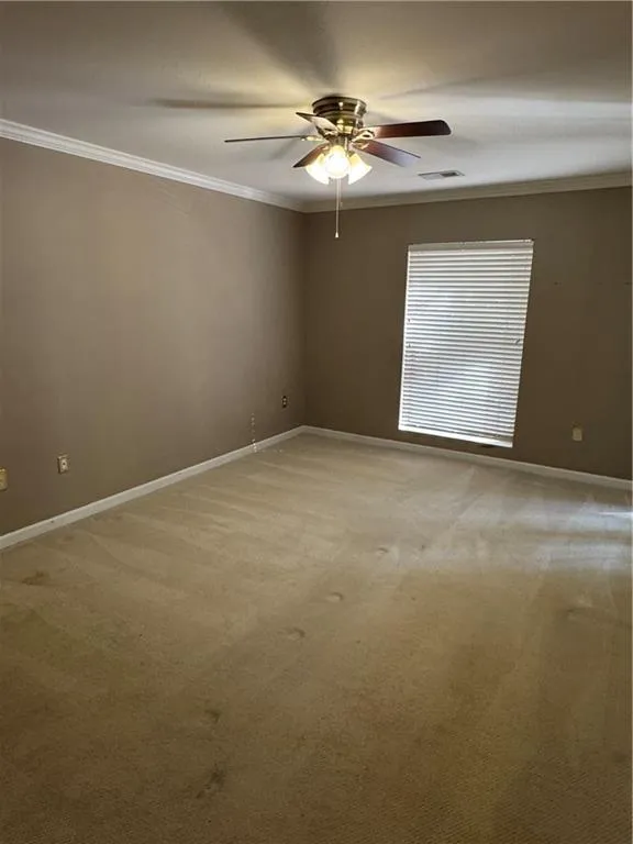 Empty room with ornamental molding, light carpet, and ceiling fan