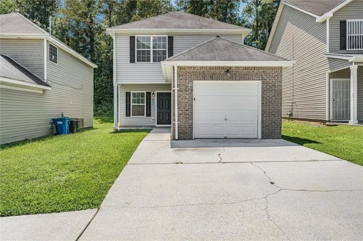 Two-story residence featuring light gray siding, dark shutters, a front entry door, an attached garage with a white door, and a concrete driveway