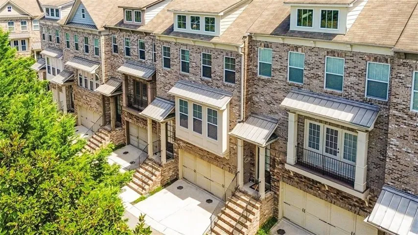 Brick exterior construction, attached garages, balcony with metal railing, dormer windows, and architectural roof shingles