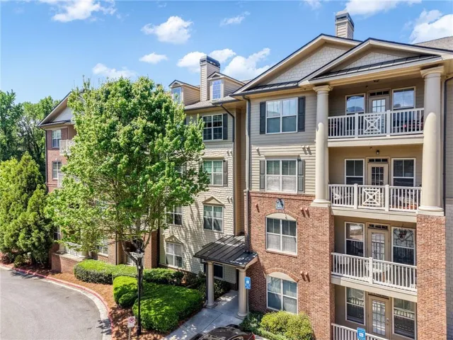 Brick and siding exterior with multiple balconies and white railings, anchored by mature landscaping and established trees
