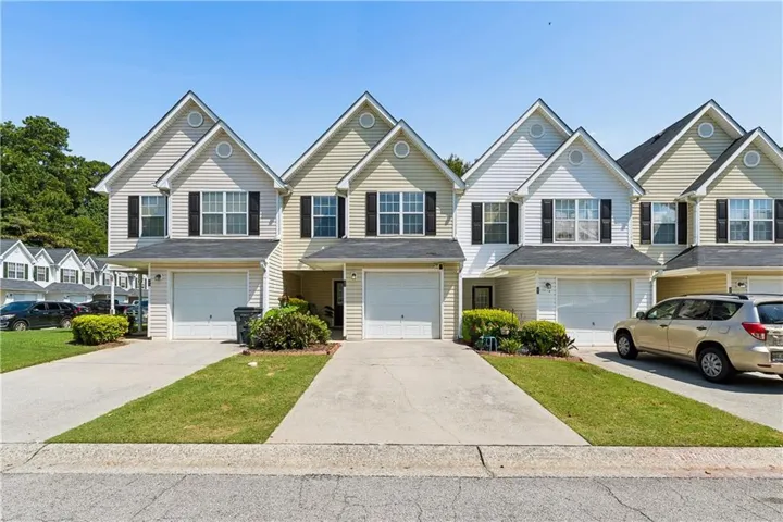 Two-story townhome with light-colored siding, black shutters, and an attached single-car garage