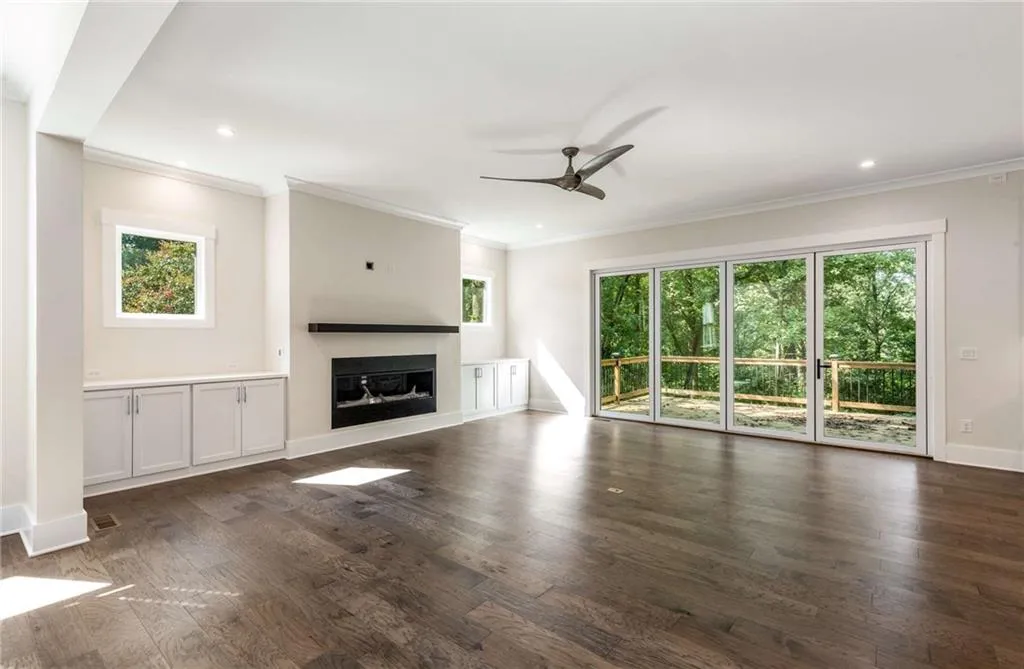 Unfurnished living room with plenty of natural light, a glass covered fireplace, crown molding, ceiling fan, and dark wood-type flooring