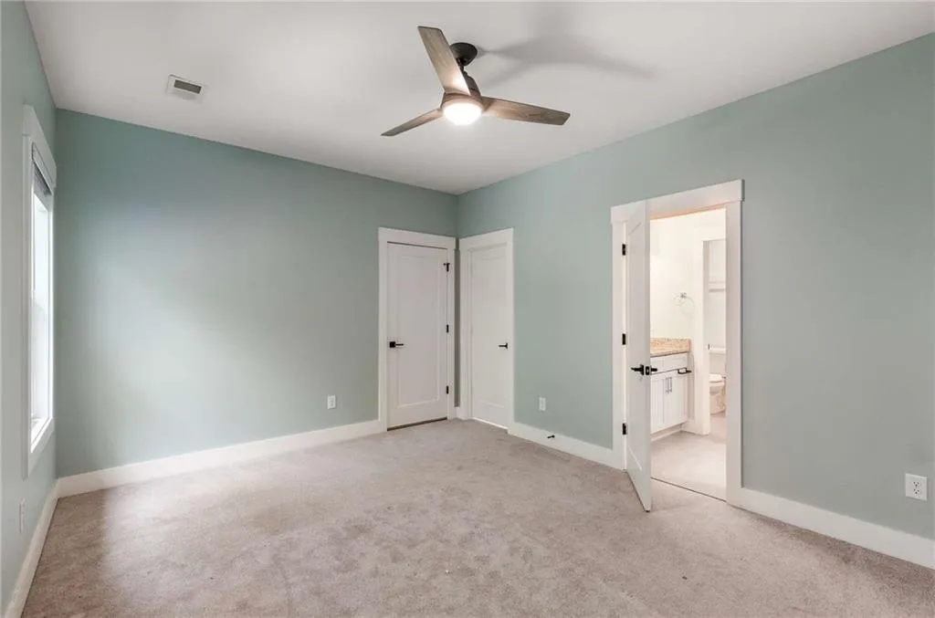 Unfurnished bedroom featuring light carpet, ceiling fan, and ensuite bathroom