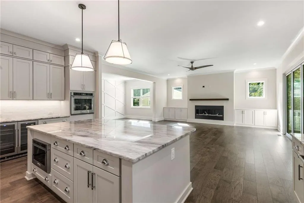 Kitchen with dark wood-style flooring, pendant lighting, a center island, light stone countertops, and beverage cooler