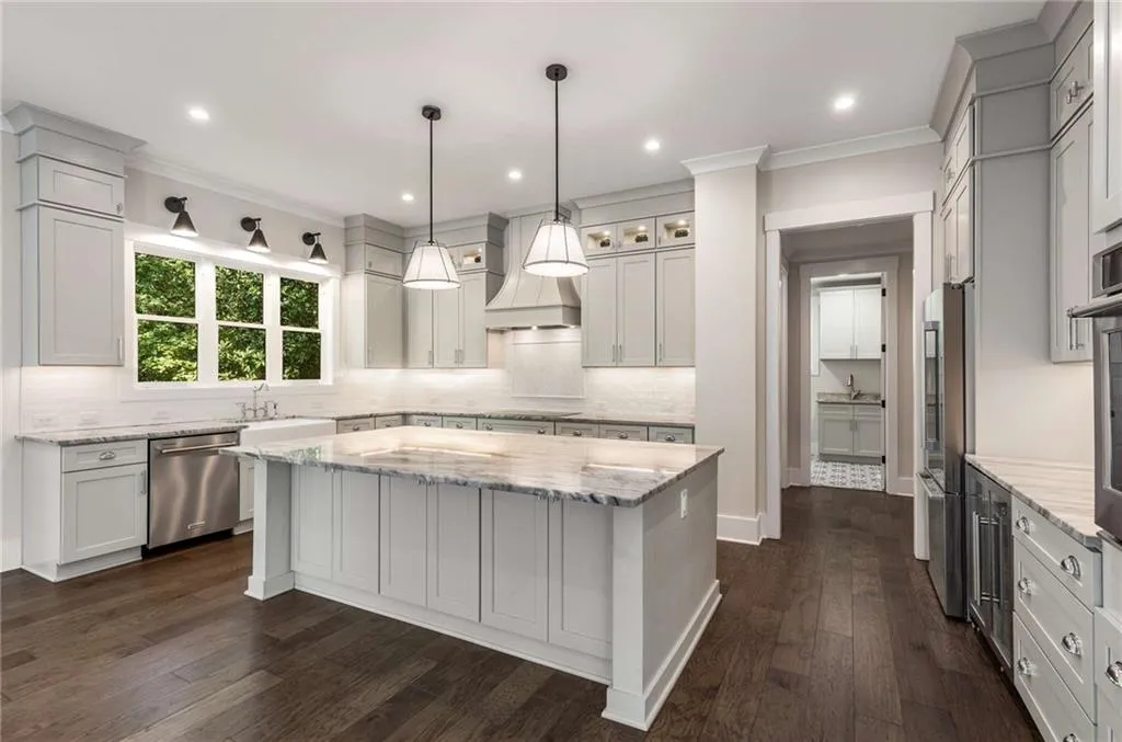 Kitchen with light stone counters, a center island, custom range hood, crown molding, and decorative light fixtures
