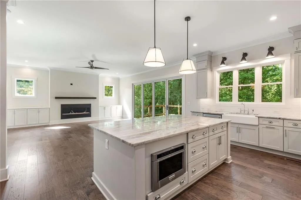 Kitchen featuring ornamental molding, light stone countertops, dark wood-type flooring, hanging light fixtures, and healthy amount of natural light