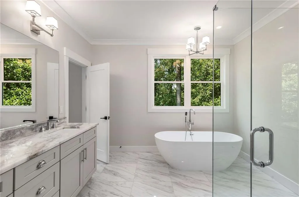 Full bathroom featuring vanity, crown molding, a freestanding tub, light marble finish floors, and a shower stall