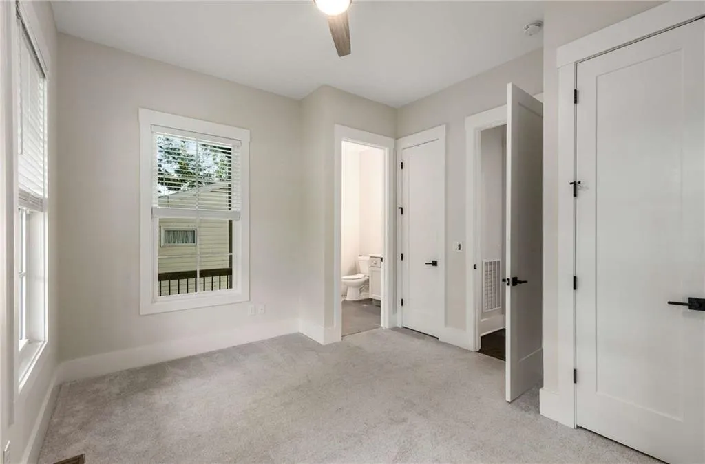 Unfurnished bedroom featuring light colored carpet, ensuite bathroom, and ceiling fan