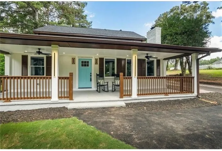 Covered front porch with wood railings and white columns, featuring a light blue front door, dark brown window shutters, and a white brick chimney