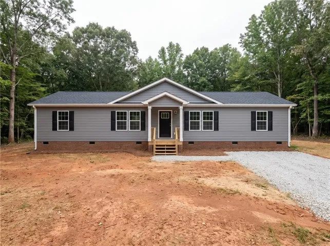 Gray siding exterior with a dark shingle roof, brick foundation, and black window shutters