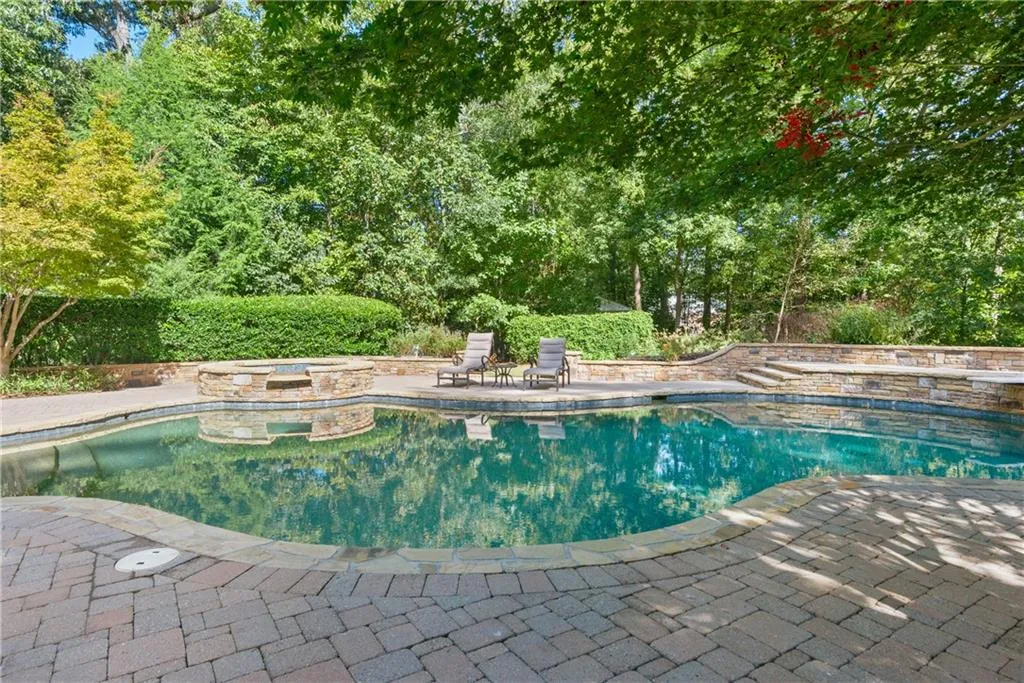 Tranquil in ground salt water pool with waterfall spa, hardcapes, and lovely, large paved pool deck surround.