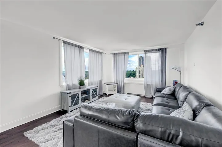 Spacious living area featuring expansive windows, dark wood-finish flooring, and white wall finishes