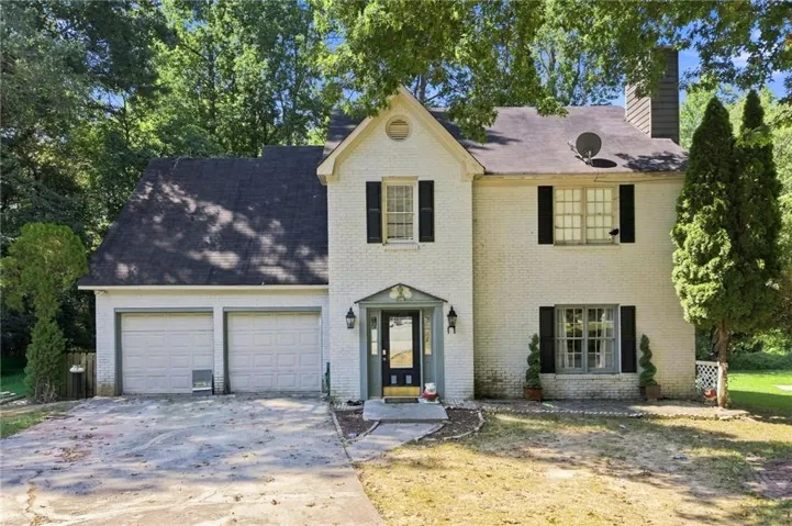 Charming Colonial-style residence featuring a brick and cream exterior with black shutters, a peaked gable roofline, and a covered front entry